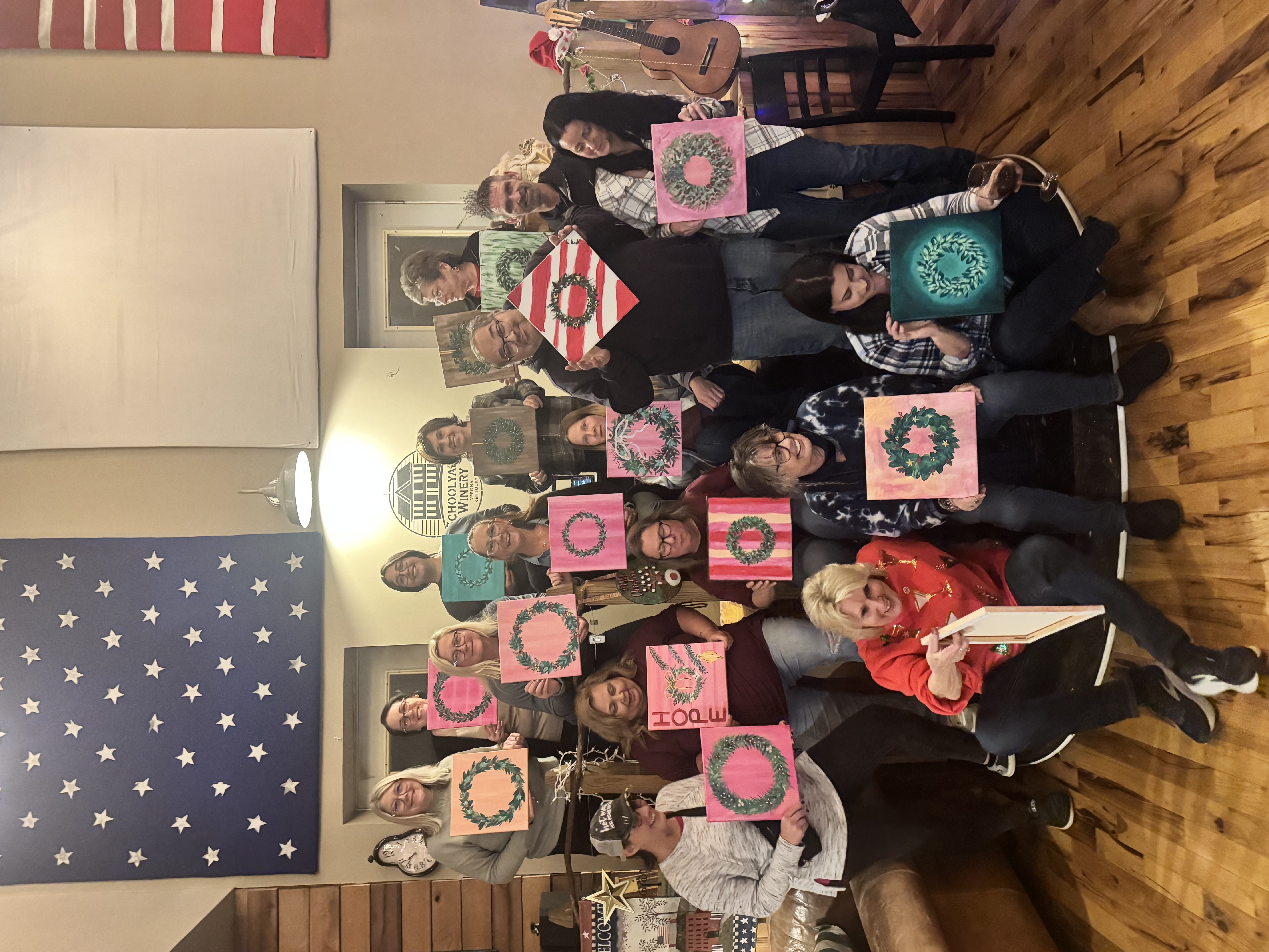 Students holding their finished holiday wreath paintings at a Paint & Pour class